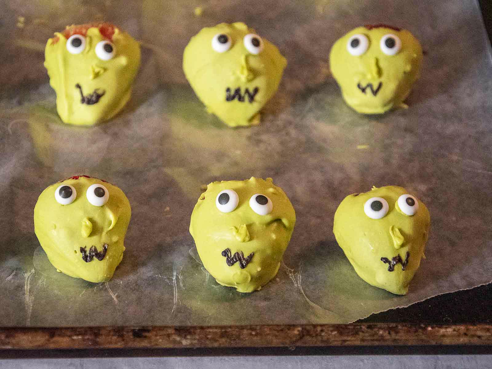 Strawberries coated in green candy with candy eyeballs and icing mouths.