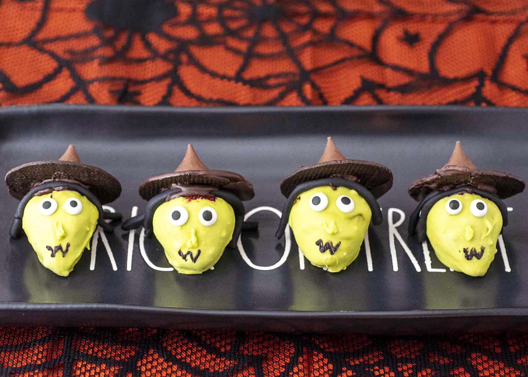 Four strawberry witches on a black rectangular serving platter.