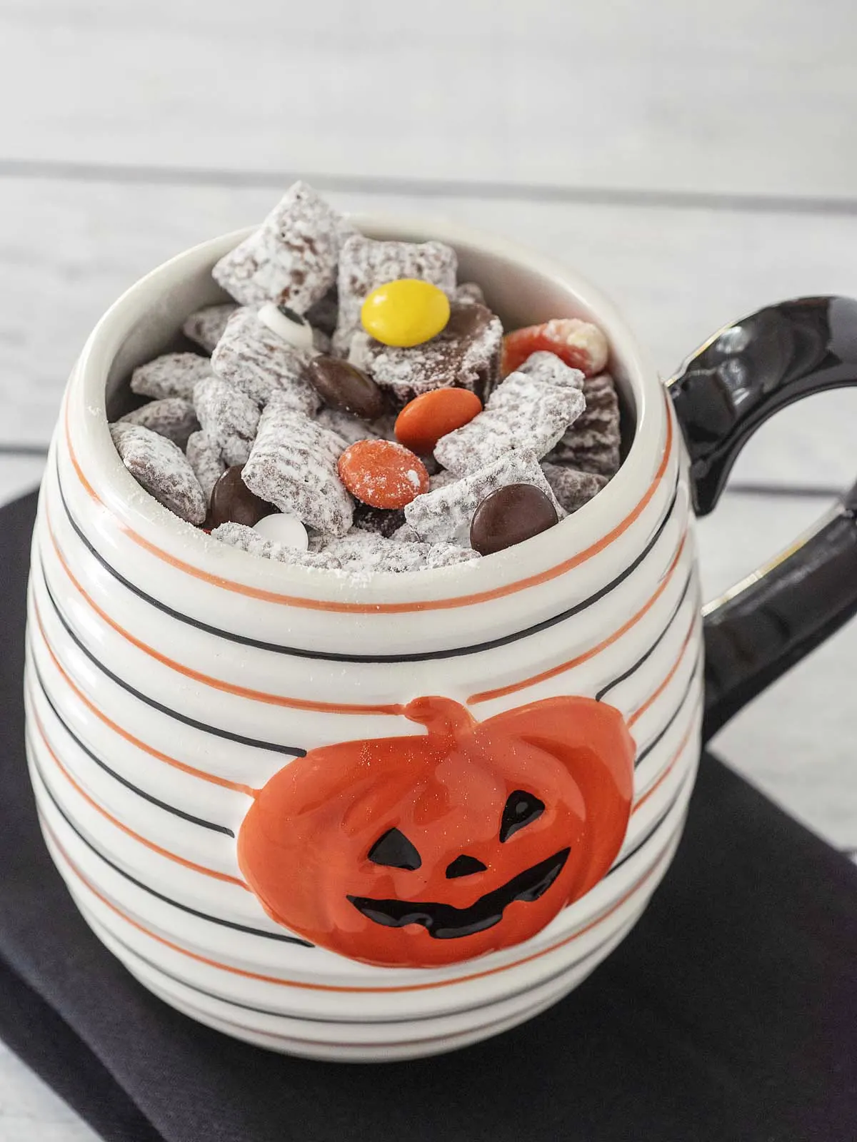 A white-with-black-and-orange striped jack-o-lantern mug full of Halloween Muddy Buddies.