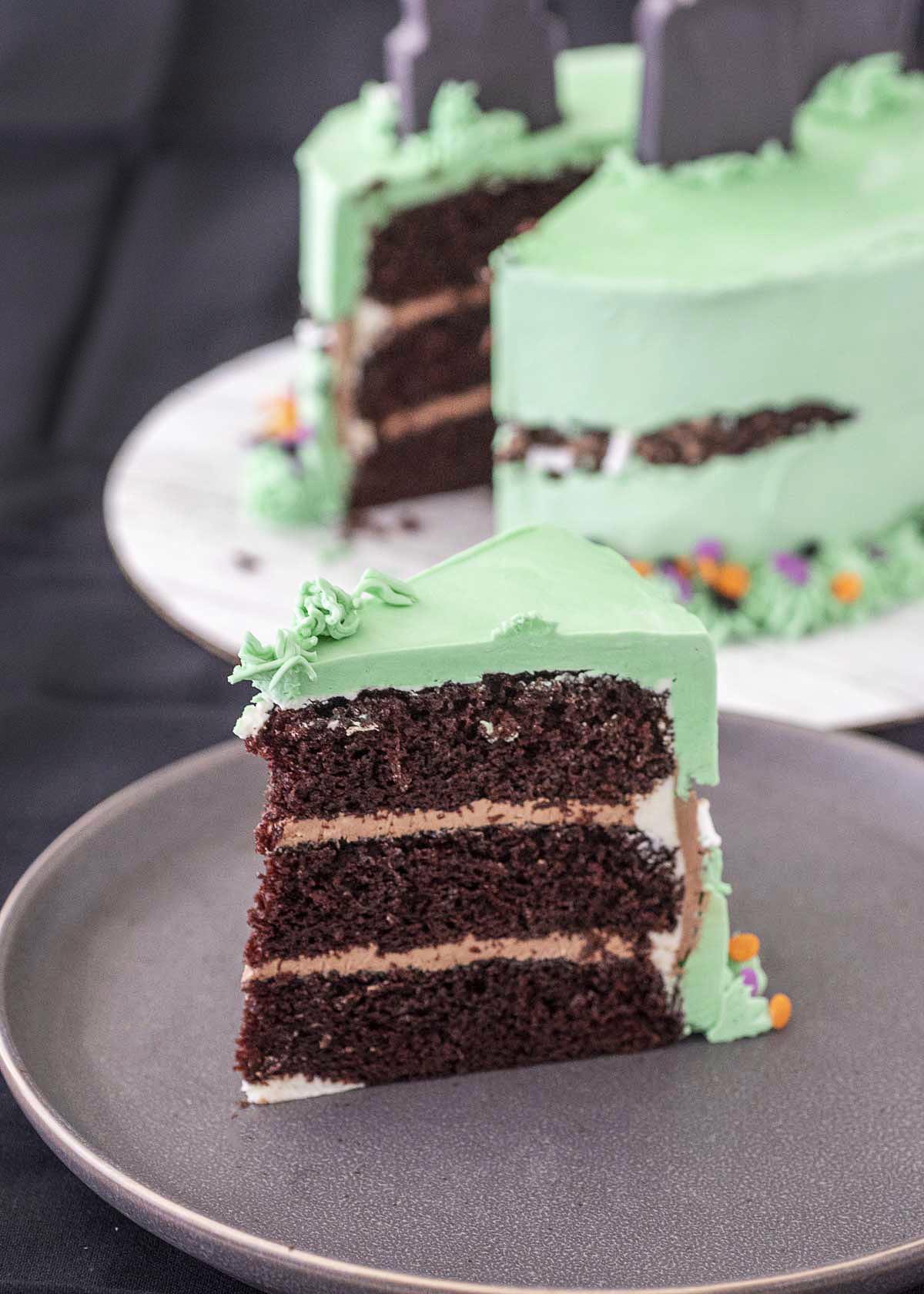 A slice of Halloween fault line cake on a gray plate in front of the rest of the cake.