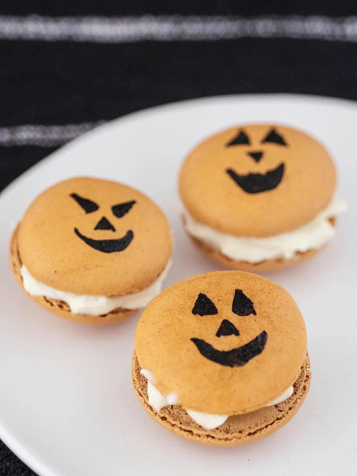 Three Halloween macarons on a white plate.