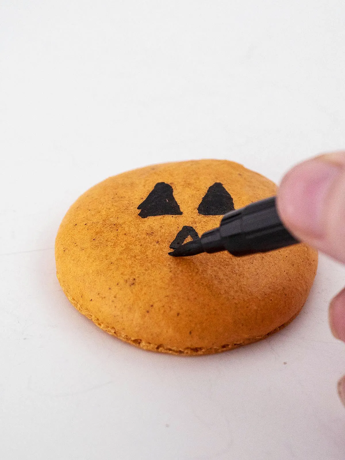 Drawing a face on a macaron shell with a food coloring pen.