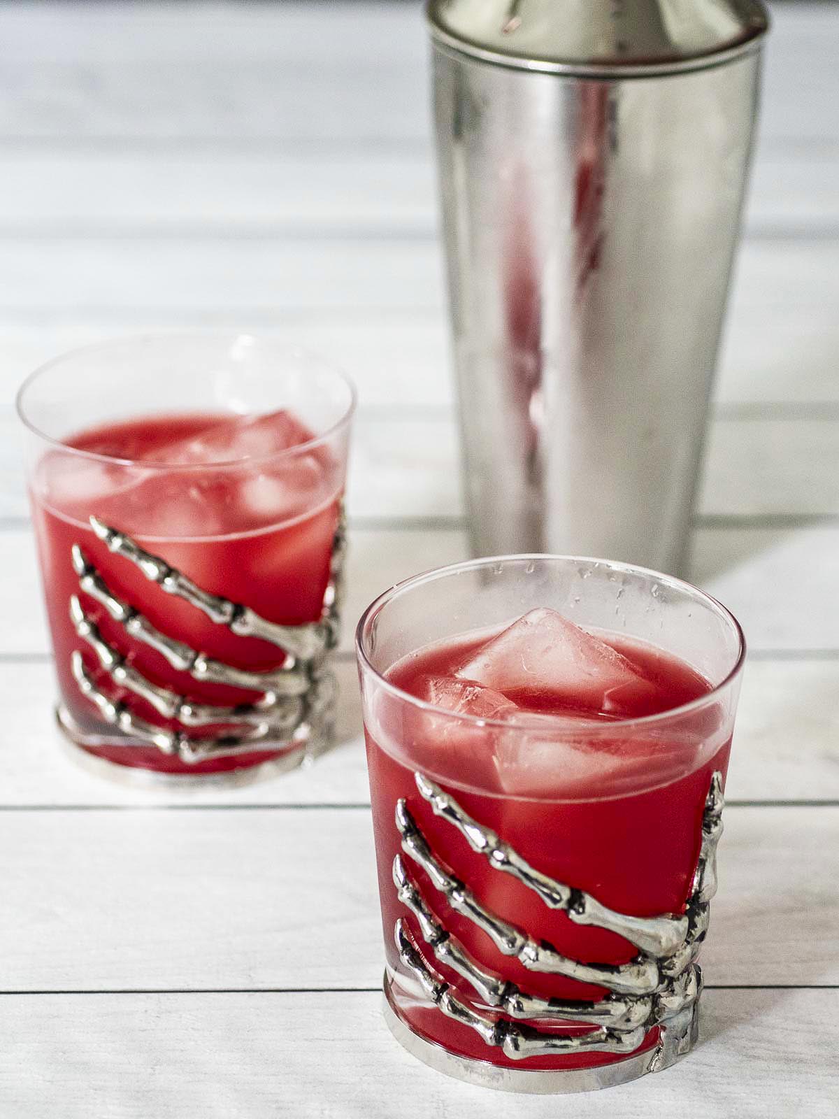 Two glasses of witches' brew in front of a cocktail shaker.