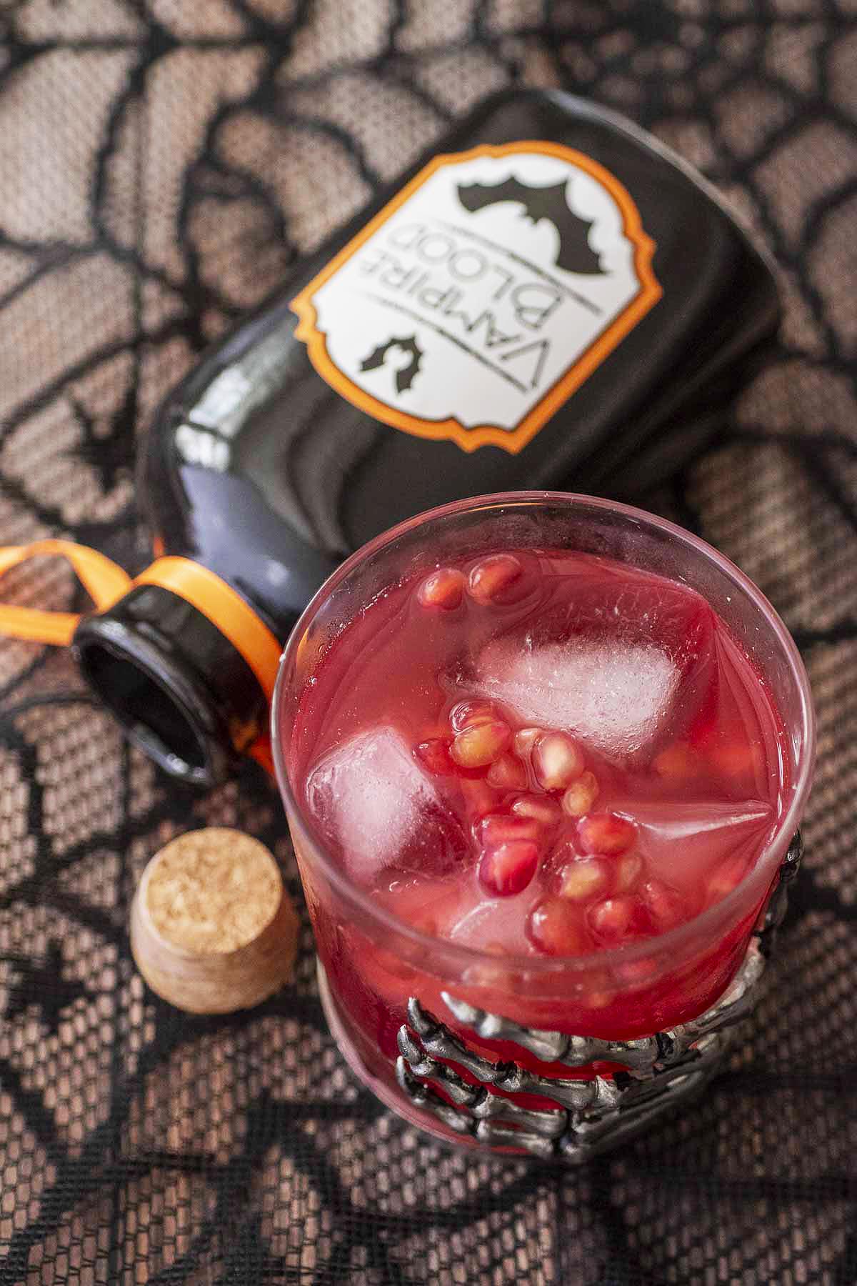 A glass of pomegranate whiskey sour with a prop bottle of vampire blood.