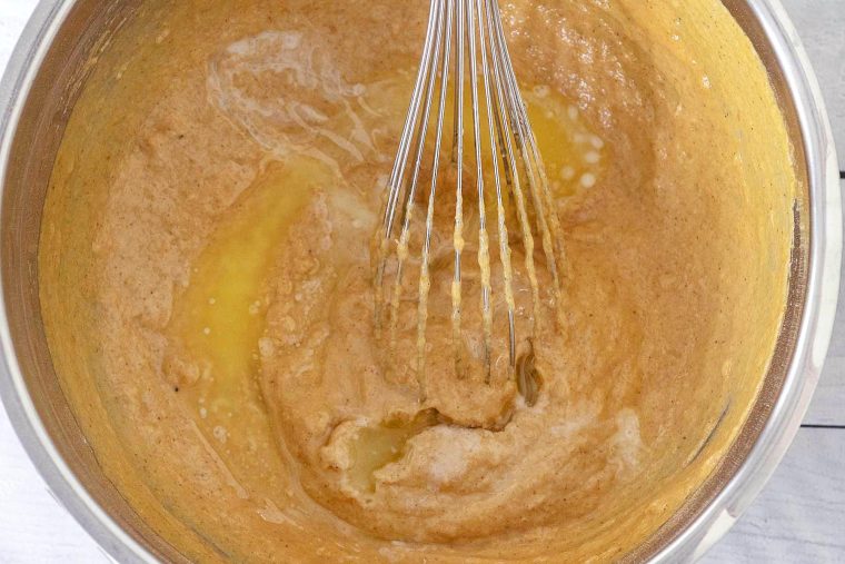 Whisking the melted butter into the pumpkin waffle batter.