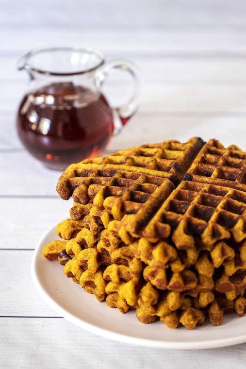 A stack of pumpkin chocolate chip waffles on a white plate.