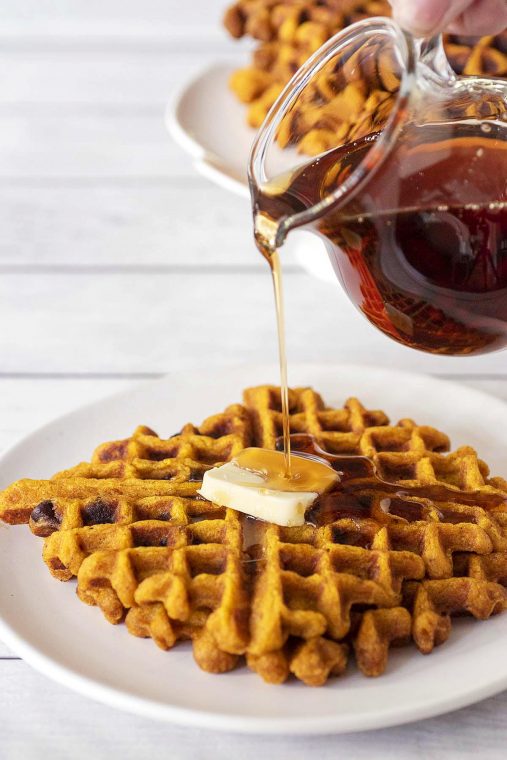 Syrup being poured onto two pumpkin chocolate chip waffles.