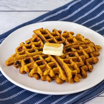 Two pumpkin chocolate chip waffles on a white plate with butter and syrup.