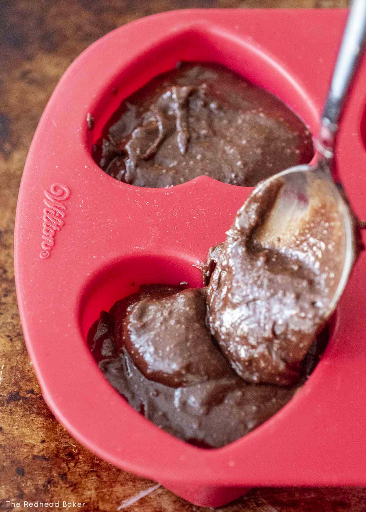 Brownie batter being spooned into a heart baking mold.