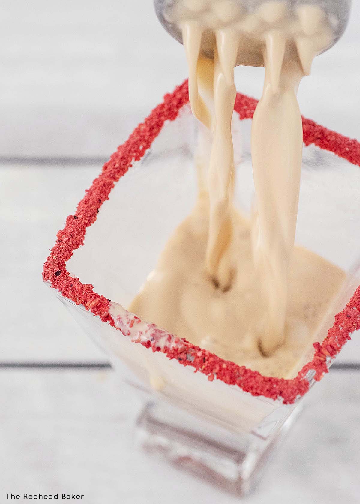 Martini mixture being poured into a strawberry-rimmed martini glass.