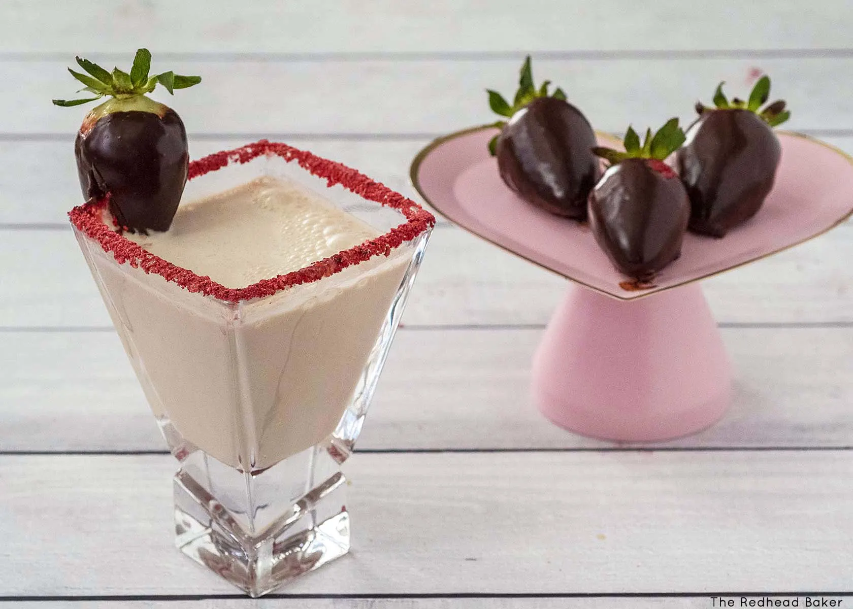 A chocolate strawberry martini next to a tray of chocolate-covered strawberries.
