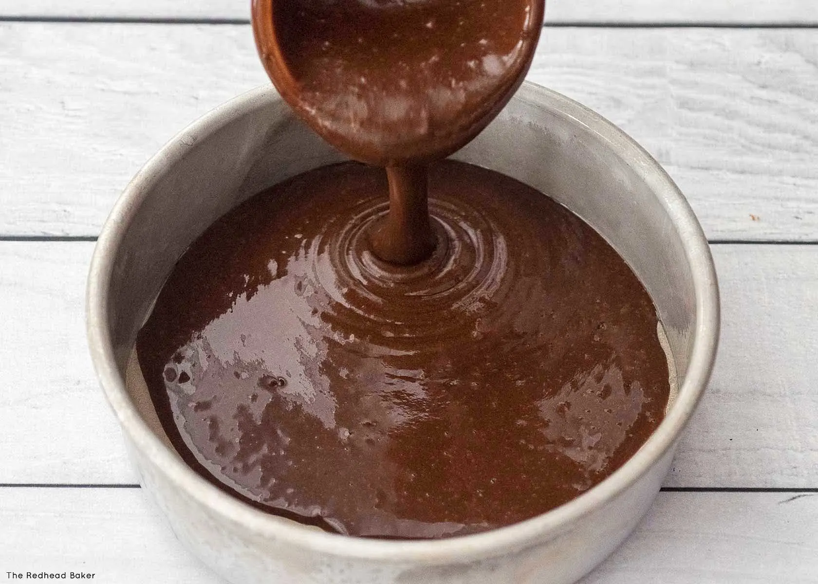 Batter being poured into a prepared cake pan.