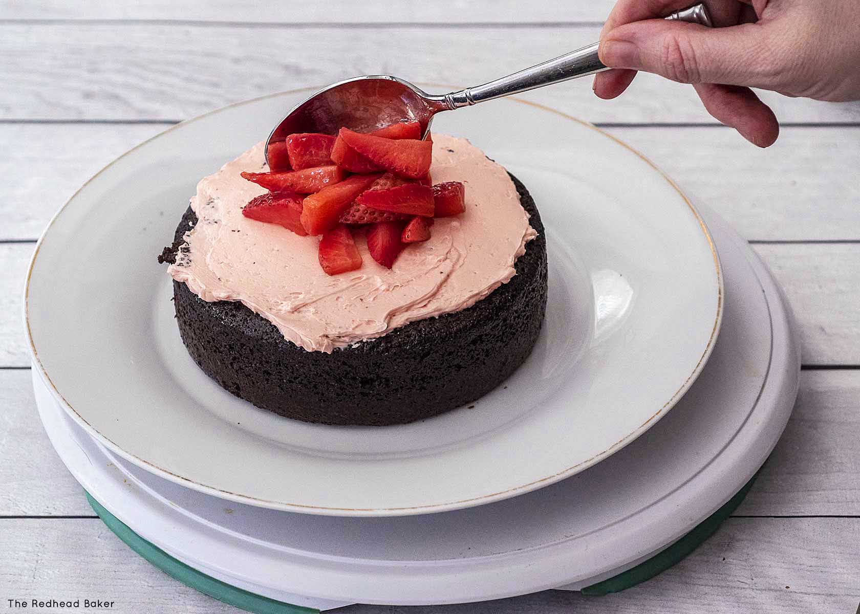 Spooning macerated strawberries onto a frosted cake layer.