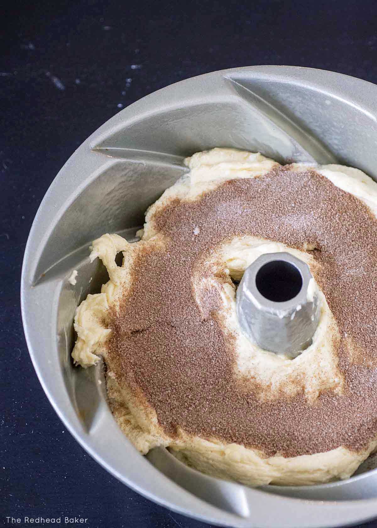 A bundt pan filled halfway with cake batter, with a layer of cinnamon sugar on top.