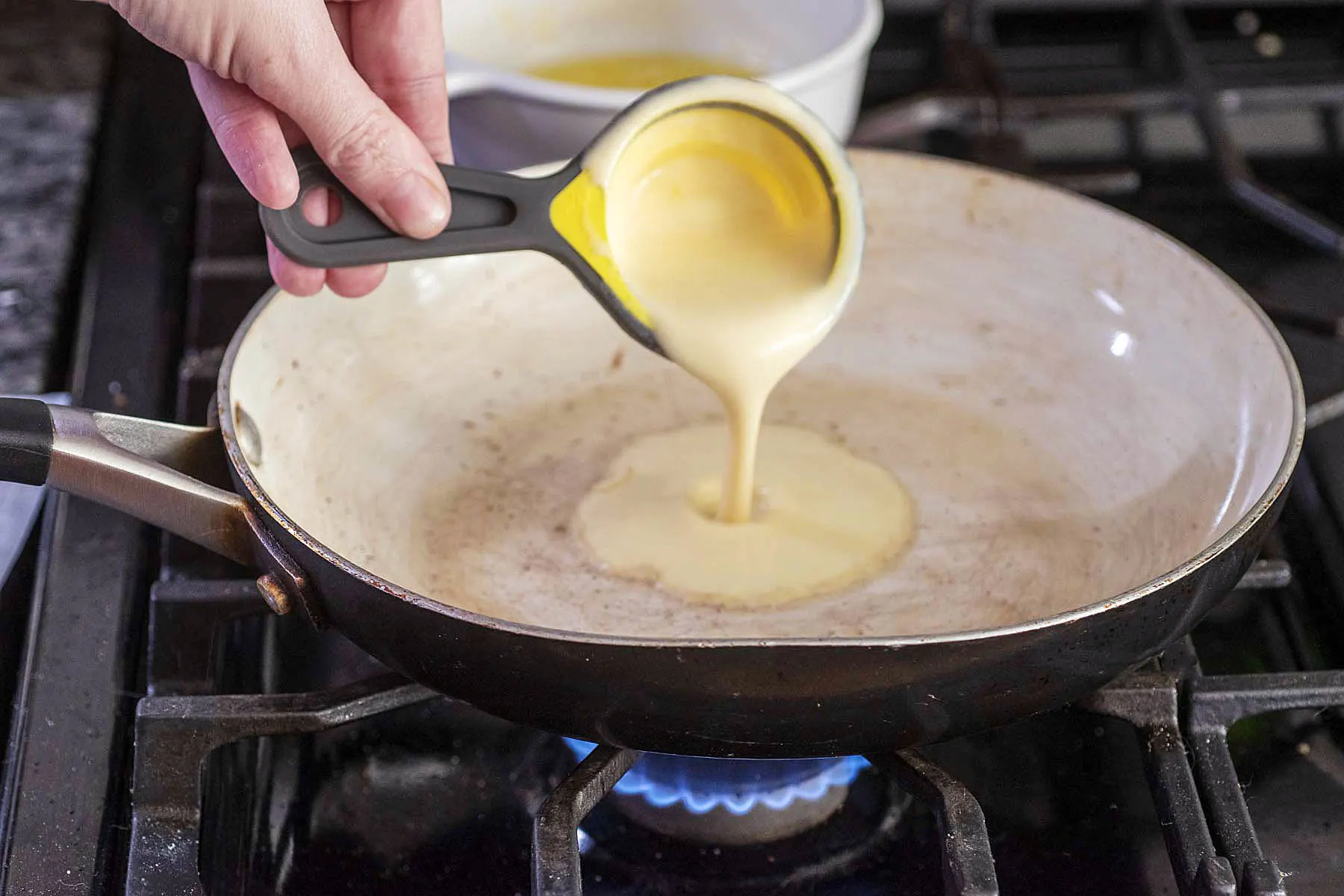 Crepe batter being poured into a nonstick skillet.