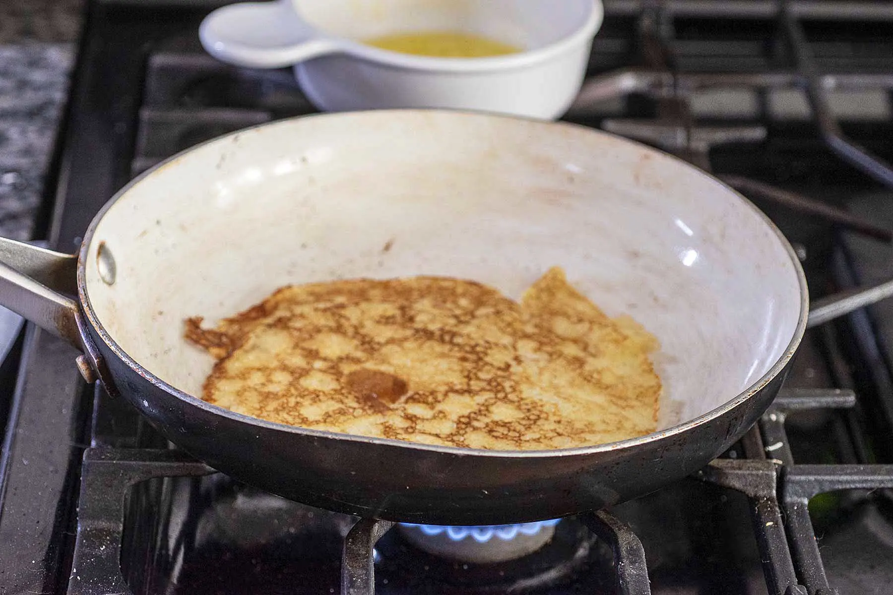 A crepe cooking on the second side in a nonstick skillet.