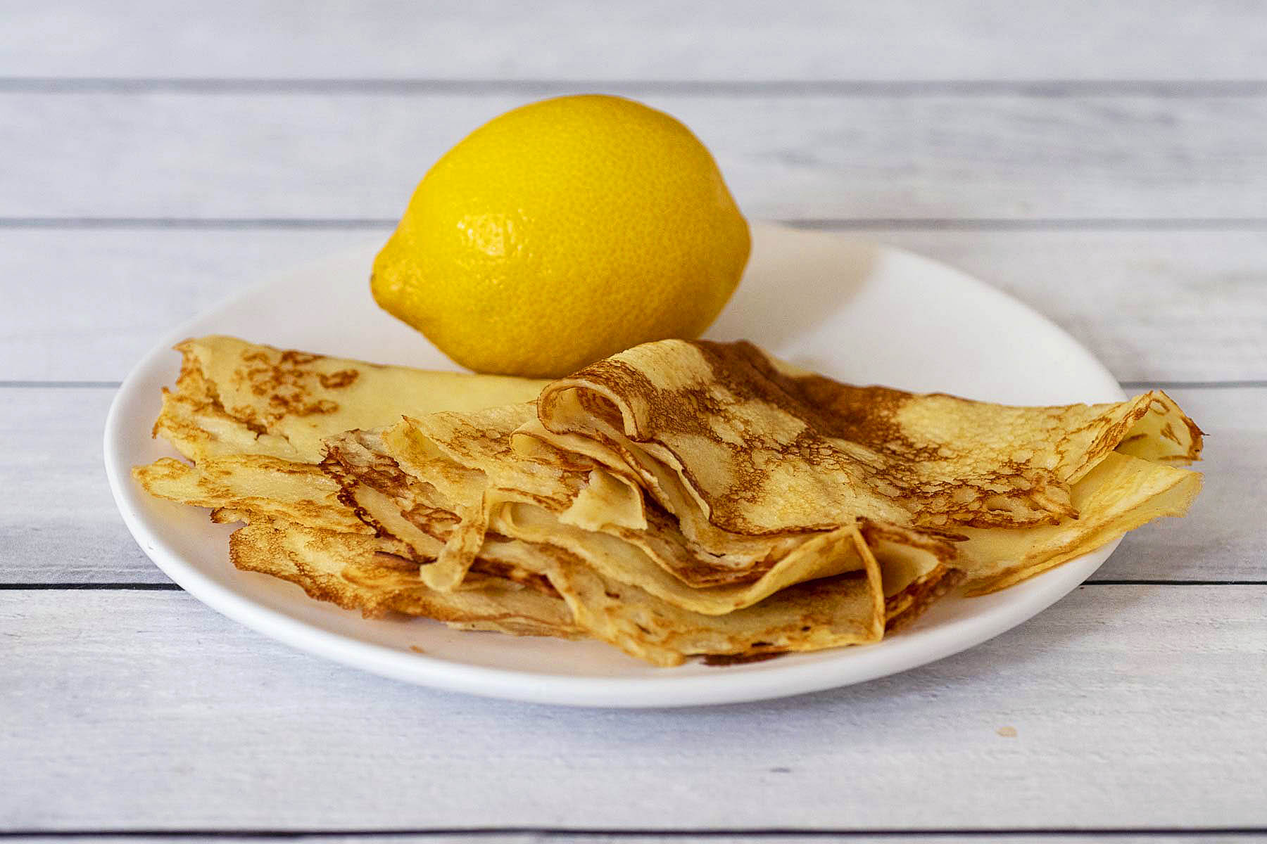 Three folded lemon crepes on a plate.