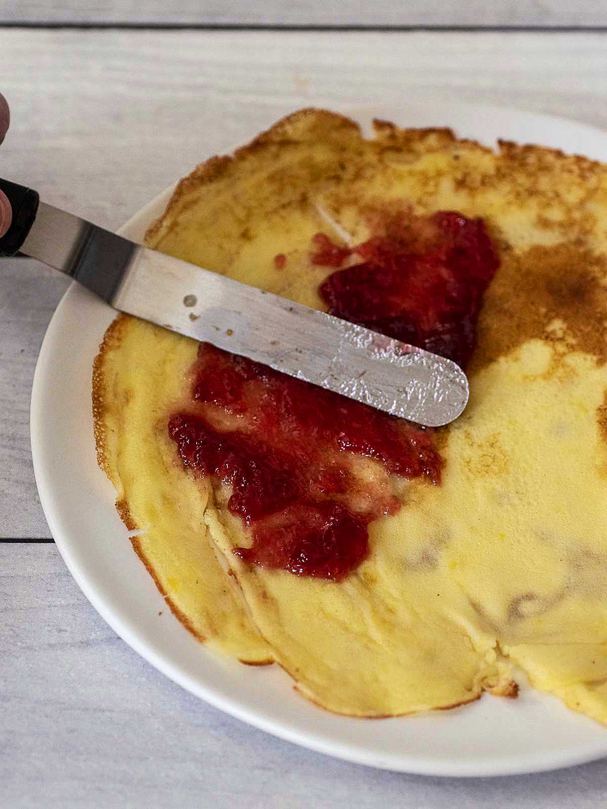 Spreading raspberry jam on a crepe.