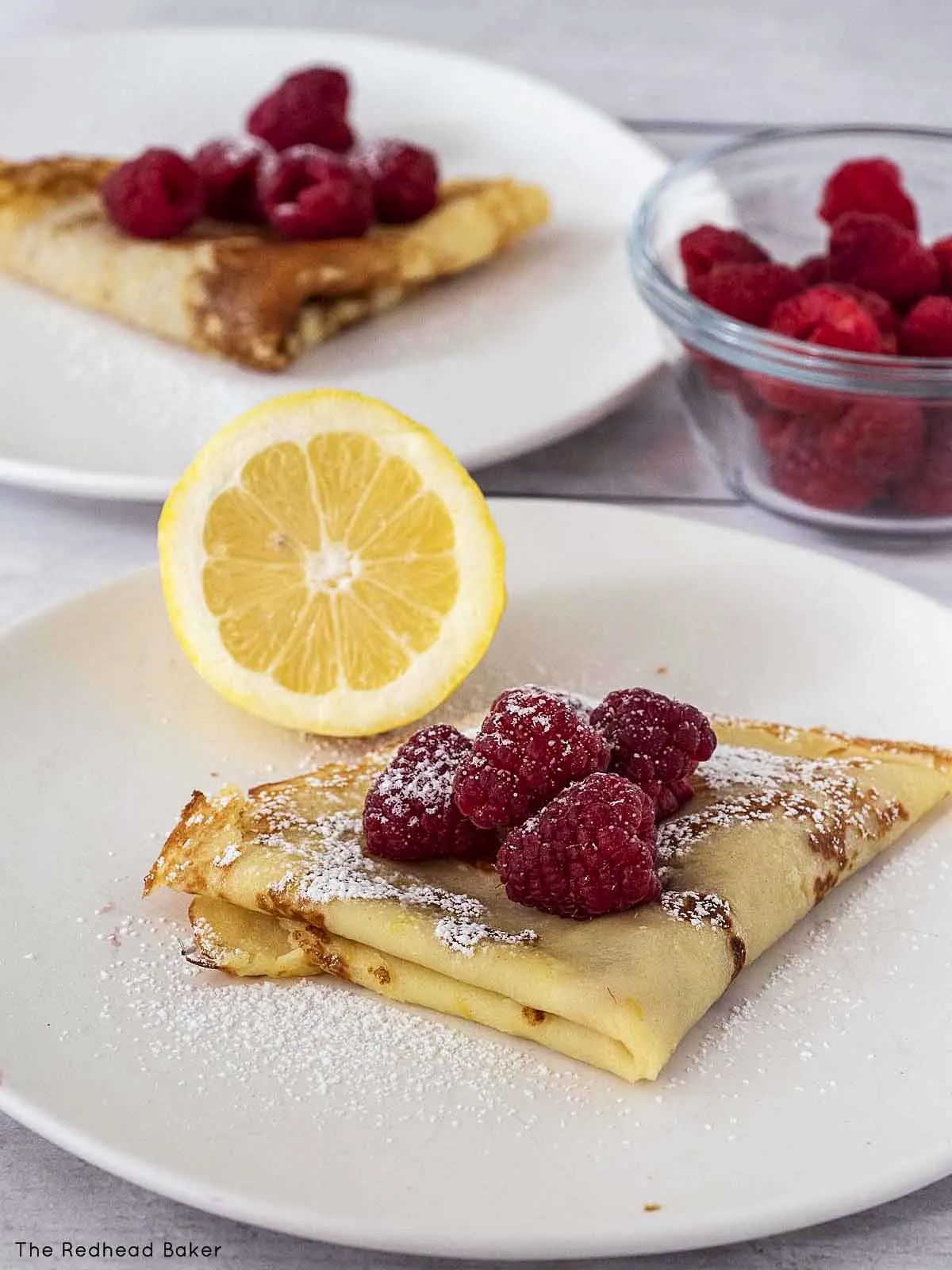 Two plates of lemon crepes with fresh raspberries.