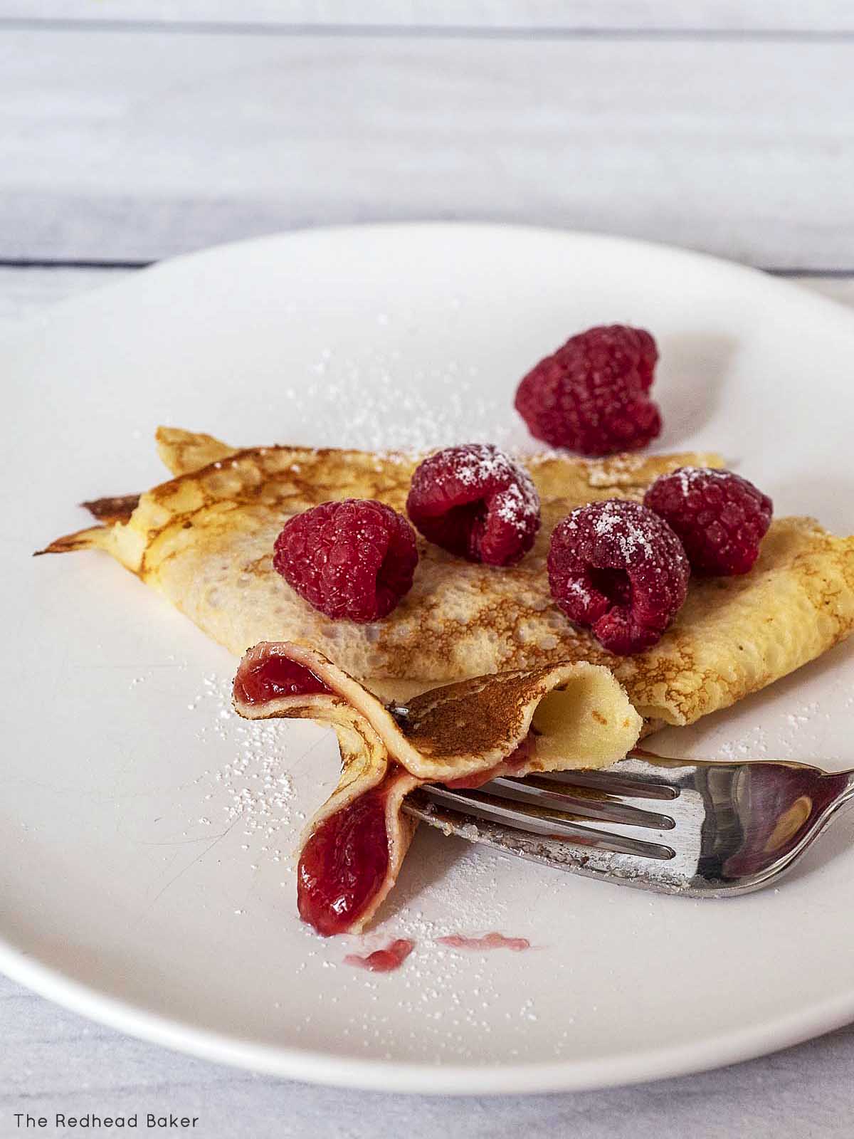 A fork holding a cut piece of lemon crepe with raspberry jam.