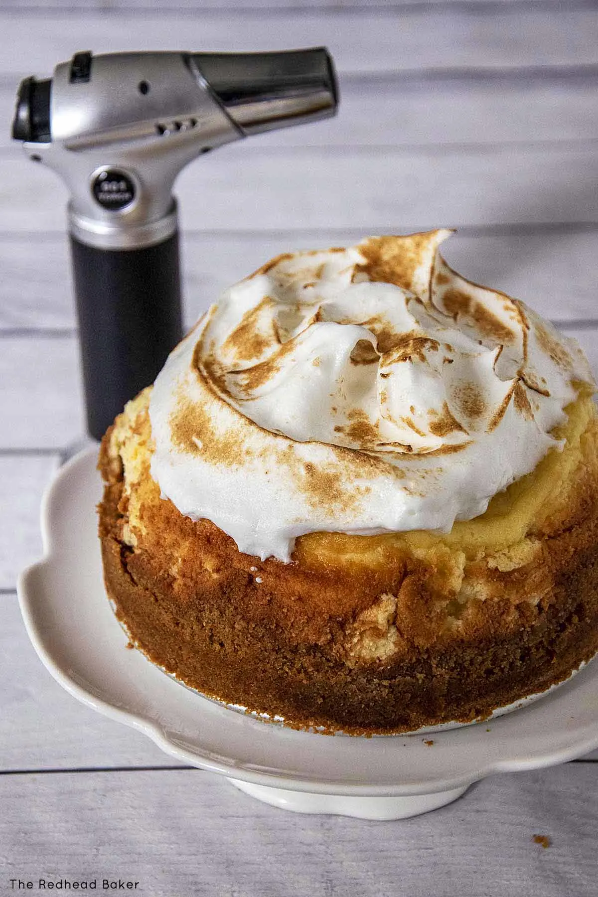 A lemon meringue cheesecake with toasted meringue in front of a butane kitchen torch.