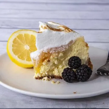 A slice of lemon meringue cheesecake with blackberries.