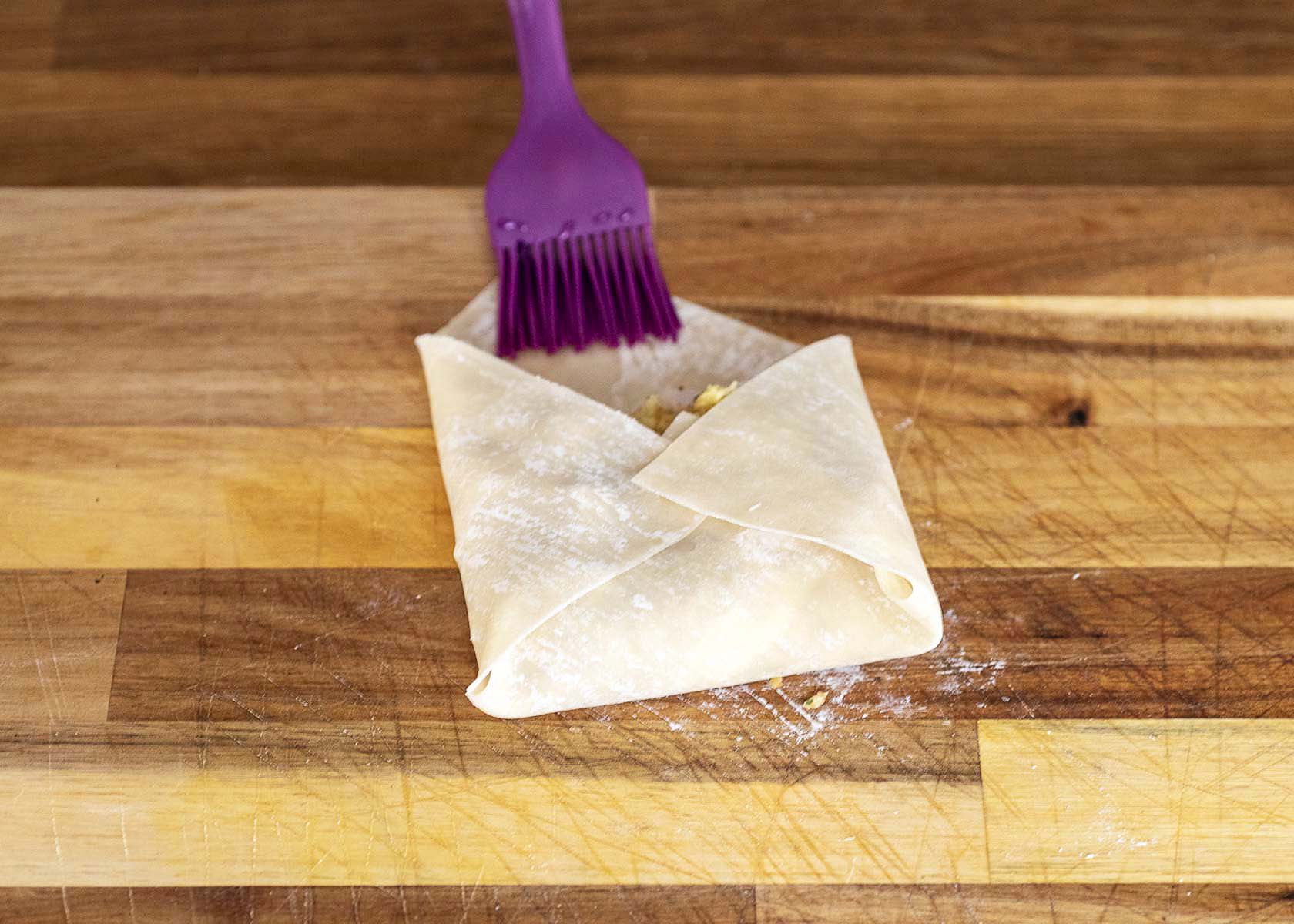 Dabbing water on the top corner before finishing rolling the egg roll.