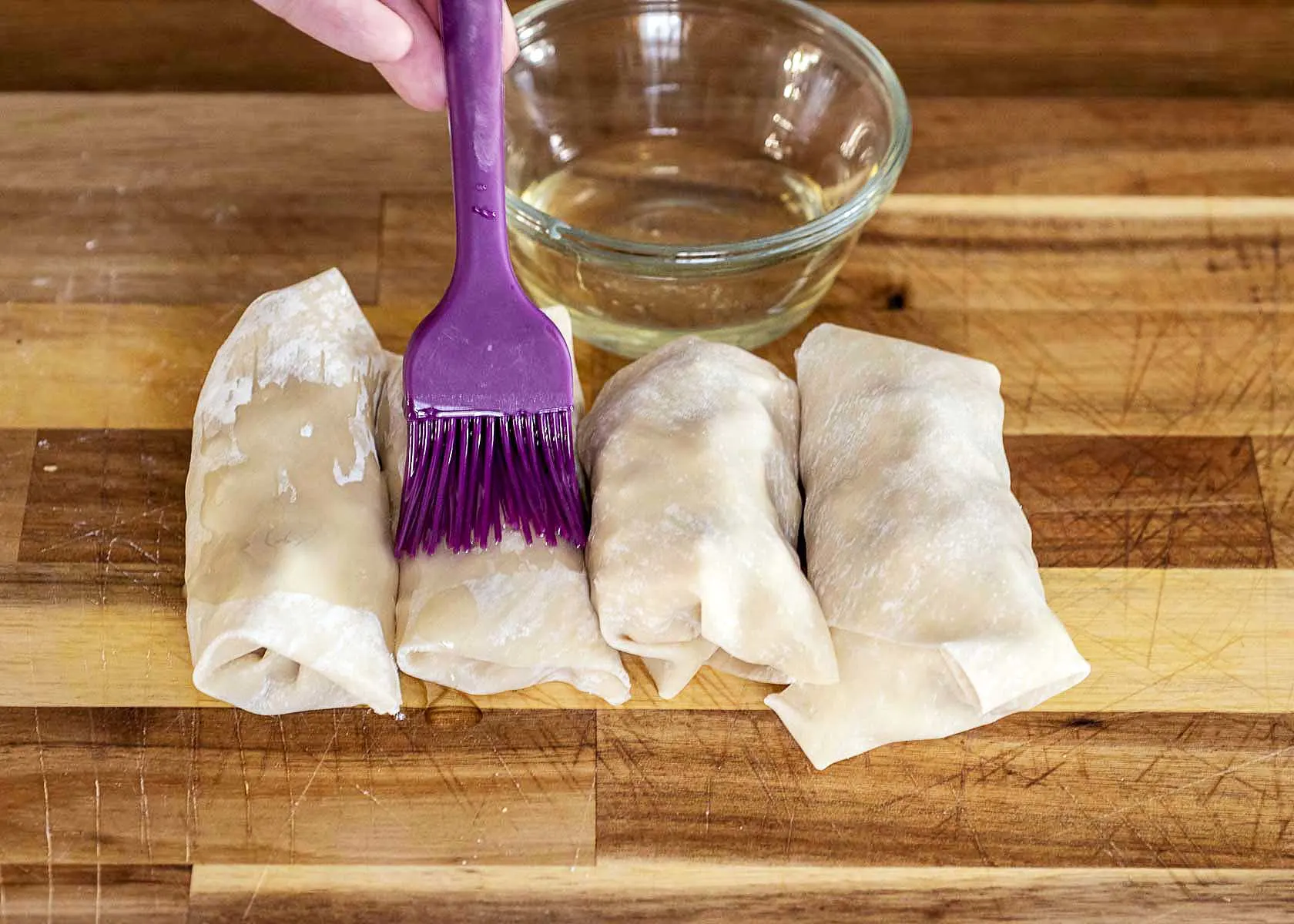 Four egg rolls being brushed with canola oil. 