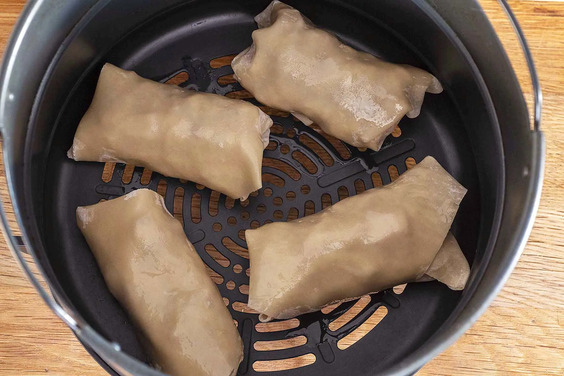 Four egg rolls in the basket of an air fryer.