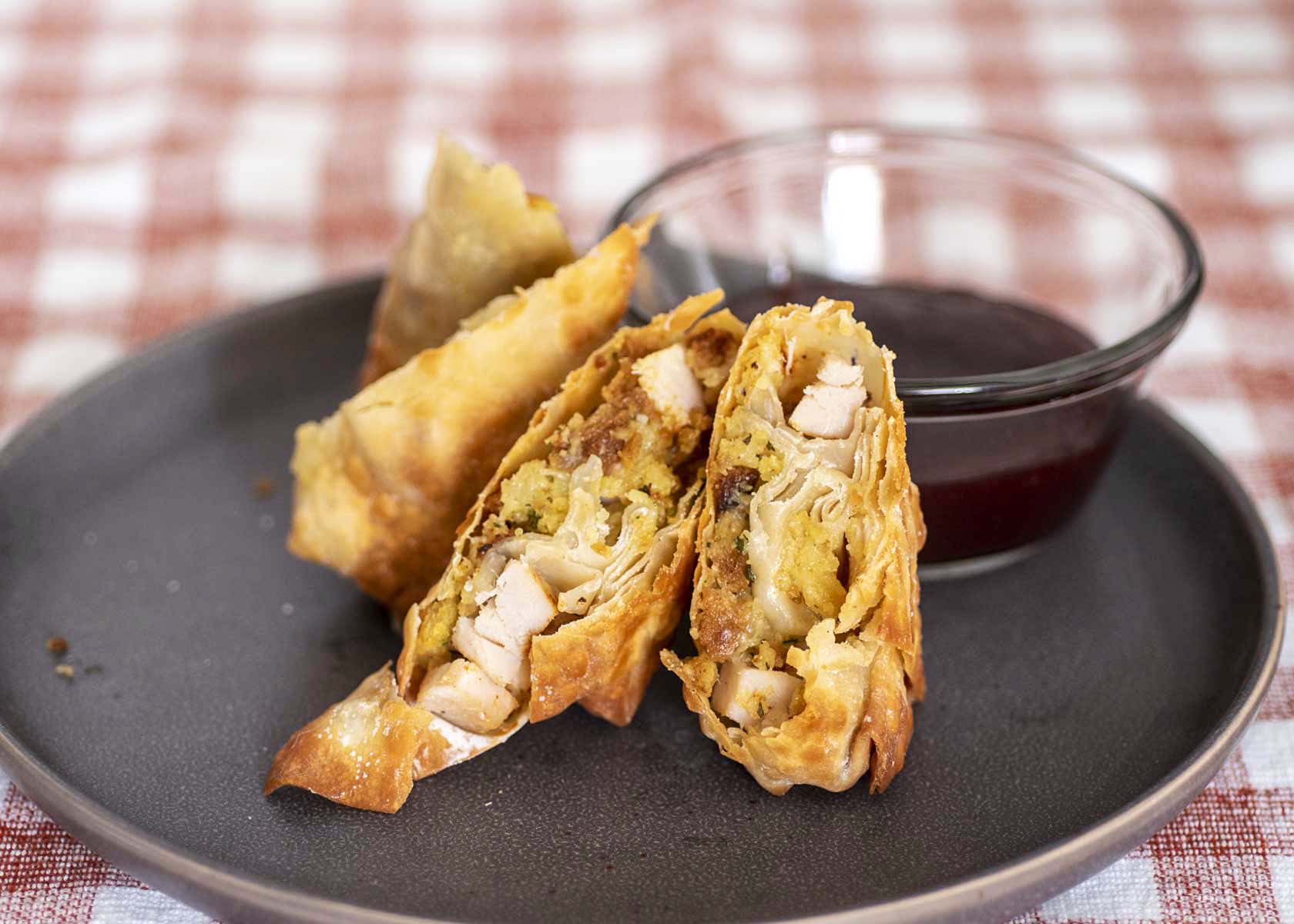 A plate of halved egg rolls with a dish of cranberry dipping sauce.