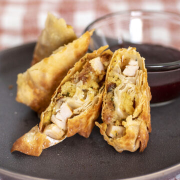 Halved egg rolls in front of a dish of cranberry dipping sauce.