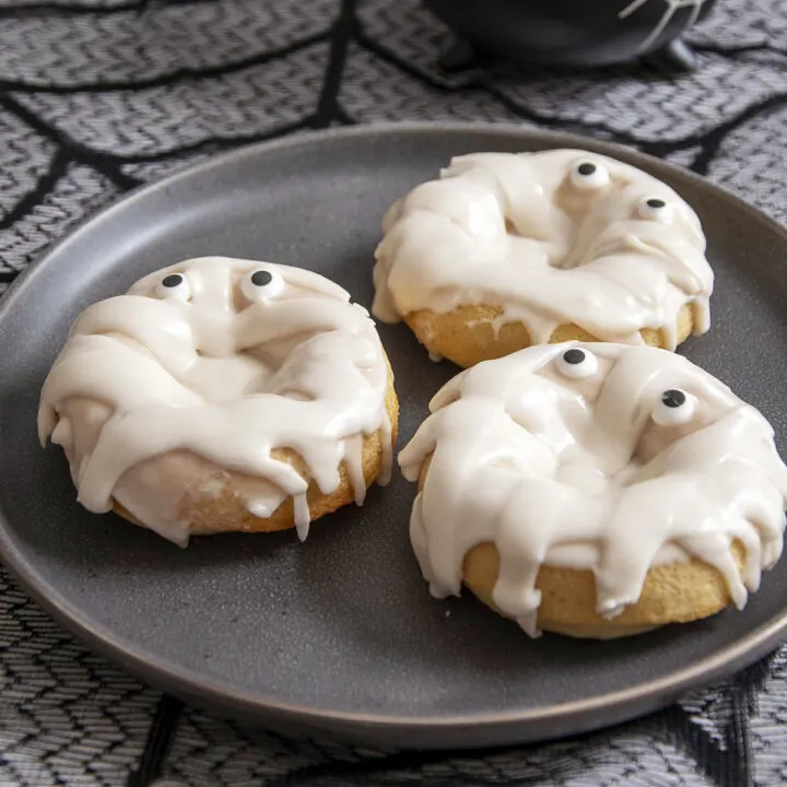 Three mummy donuts on a black plate.