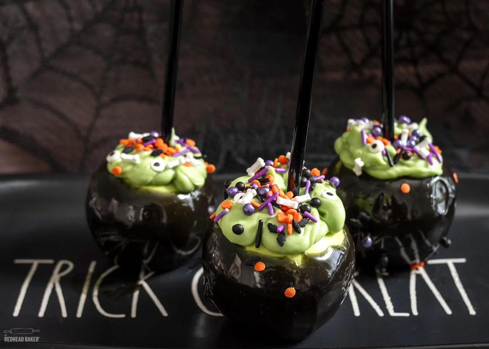 Three cauldron caramel apples on a black Halloween serving tray. 