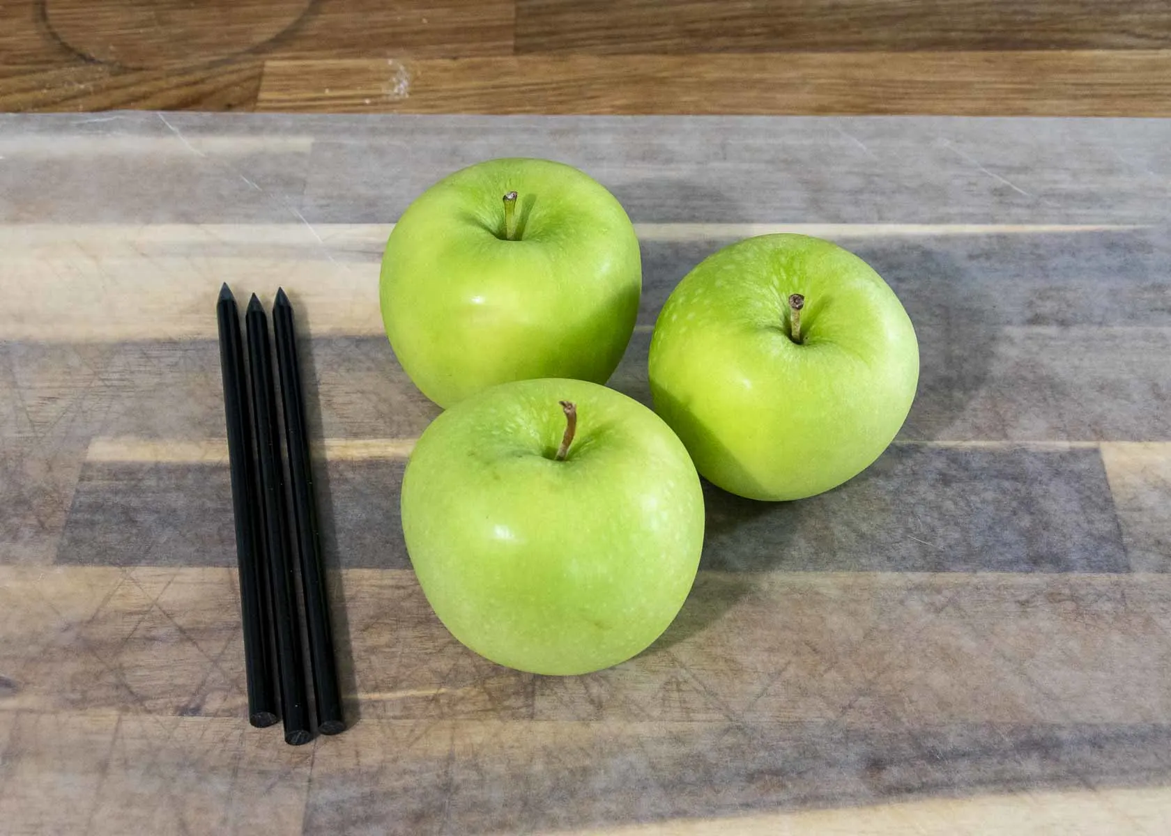 Three apples and three sticks on a wax-paper-lined cutting board.