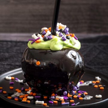 A cauldron caramel apple on a black plate.