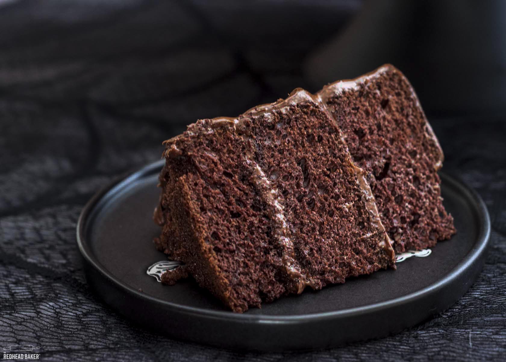 A slice of devil's food cake on a black plate.