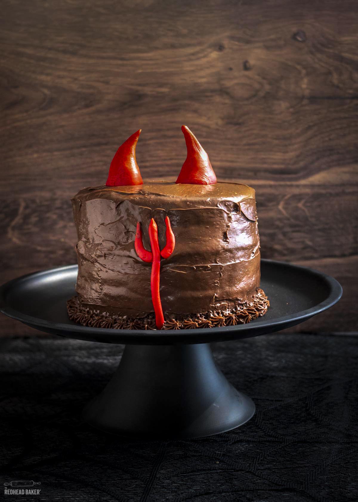 A devil's food cake with horns and a trident on a black cake stand. 