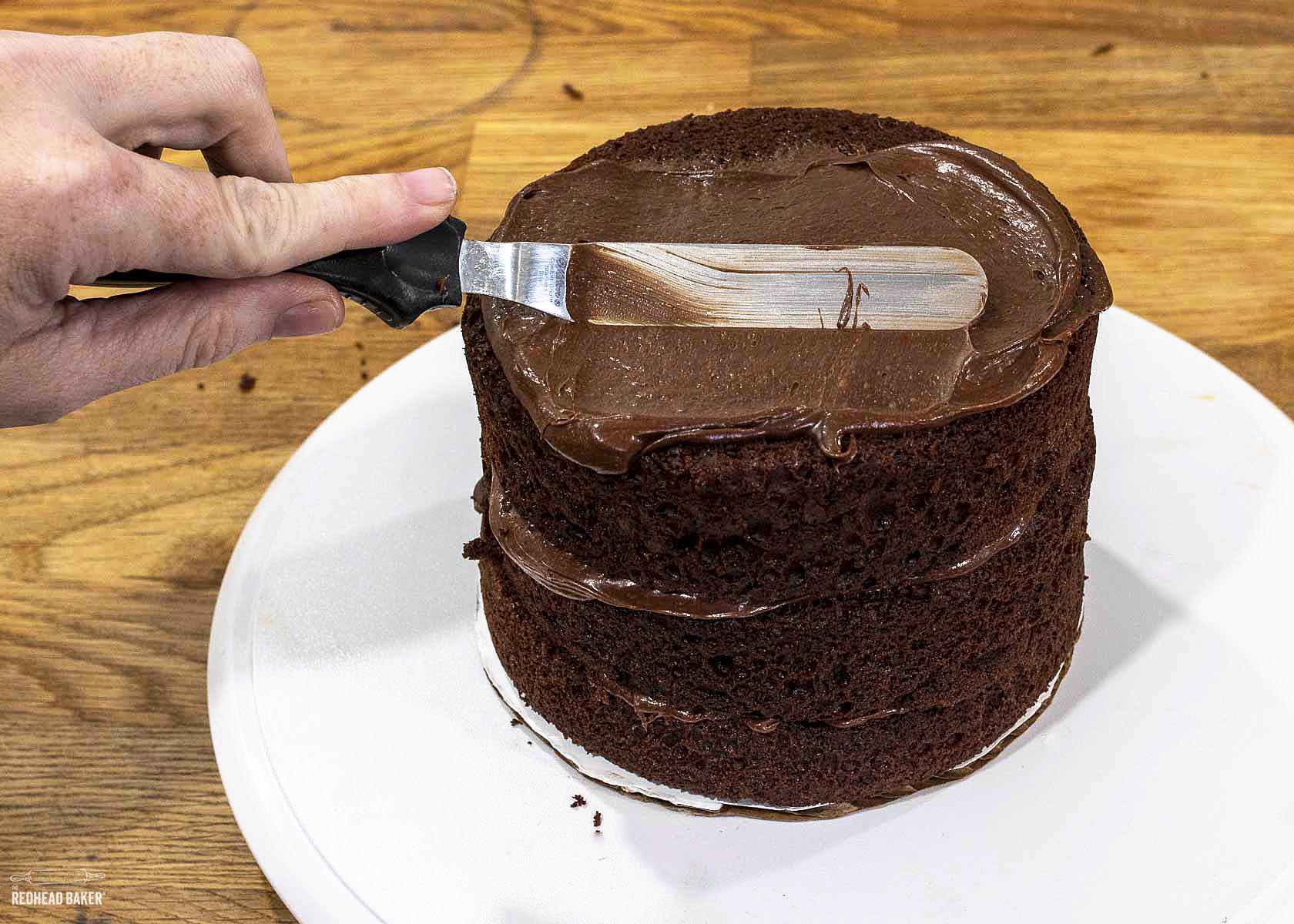 Spreading a thin layer of frosting crumb coat onto a stacked cake.