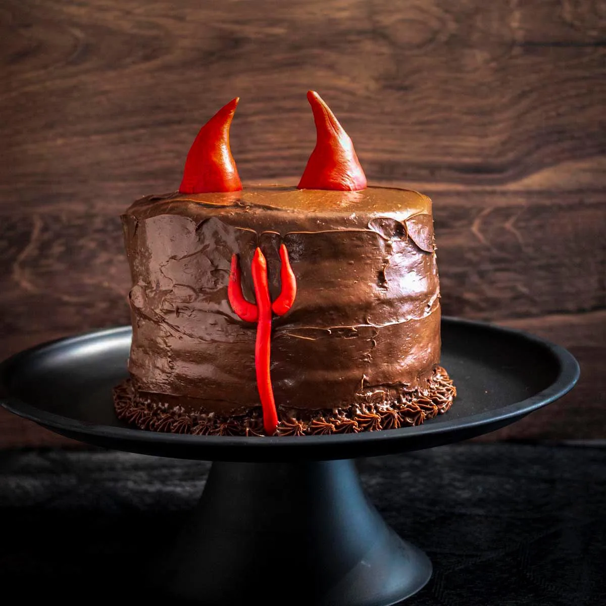 A devils food cake on a black cake stand.