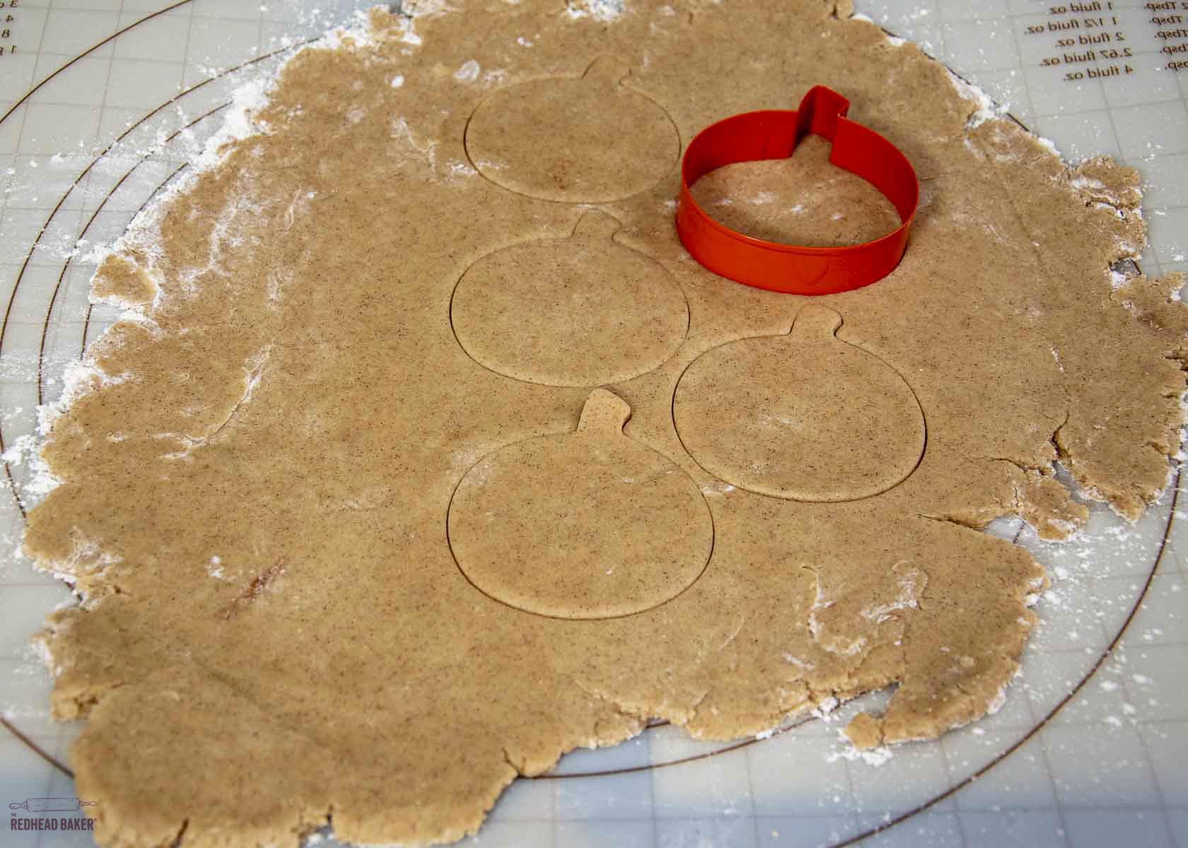 A sheet of cinnamon cookie dough with pumpkin shapes cut out.