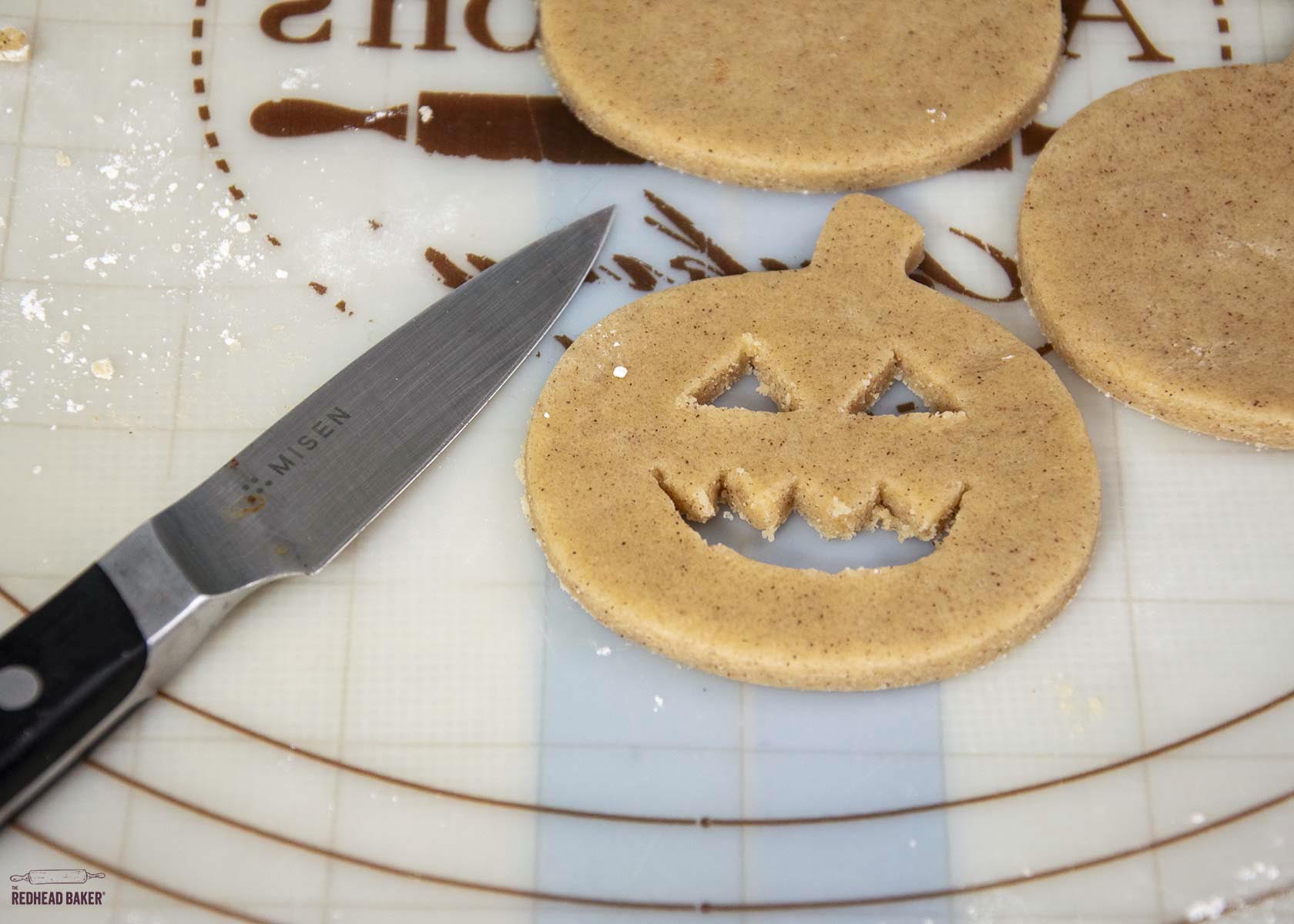 A pumpkin cookie with eyes and mouth cut out, with a paring knife to one side. 