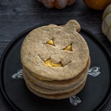 A stack of jack-o-lantern sandwich cookies on a black plate.
