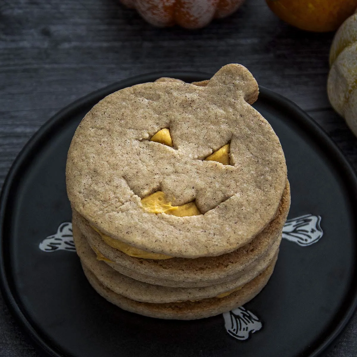 A stack of jack-o-lantern sandwich cookies on a black plate.