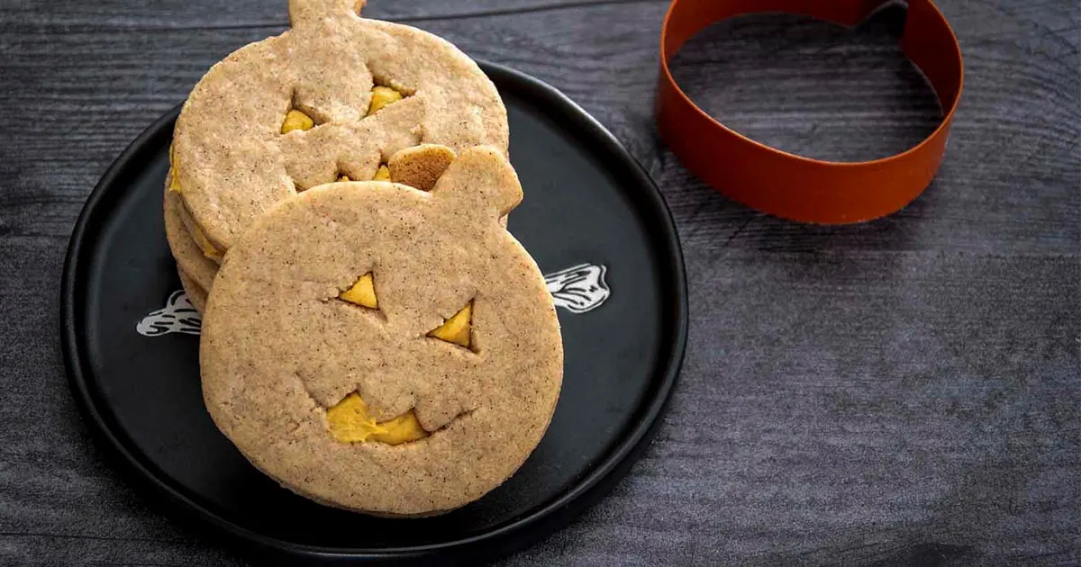 Three pumpkin sandwich cookies on a black plate.