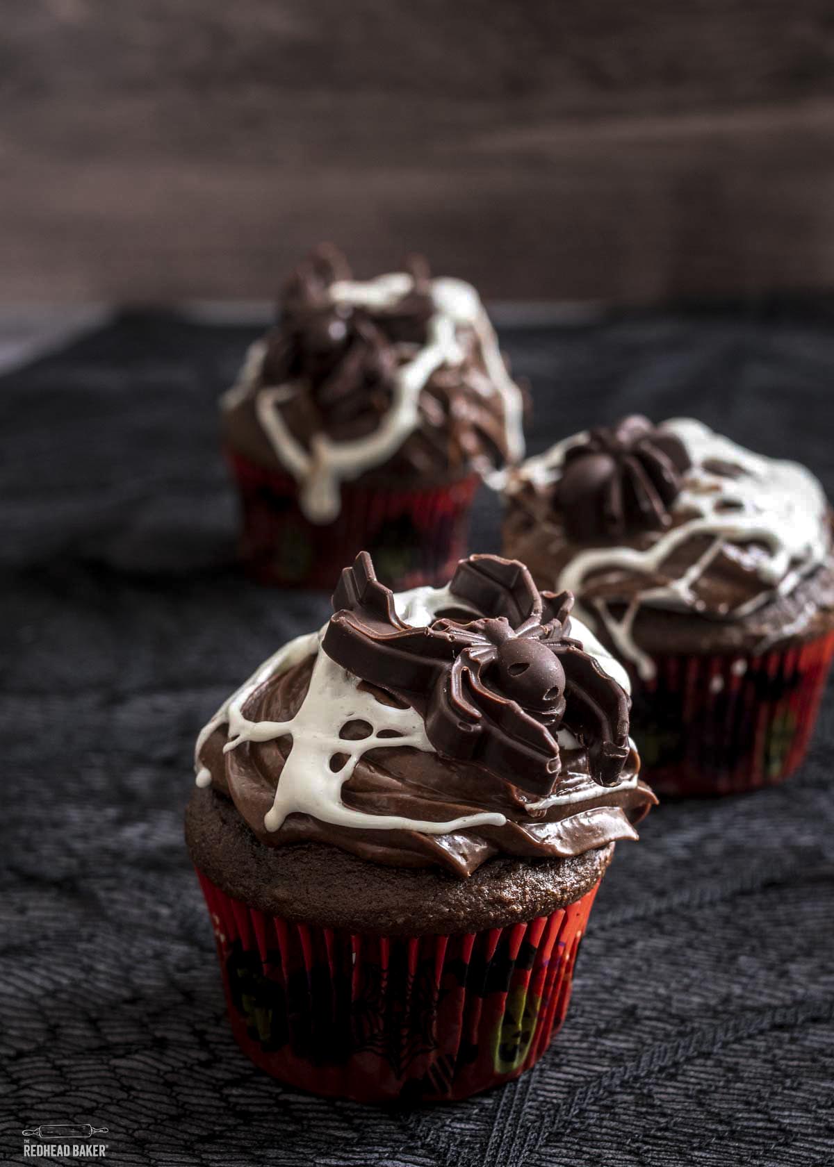 Three chocolate cupcakes with marshmallow web and candy spiders.