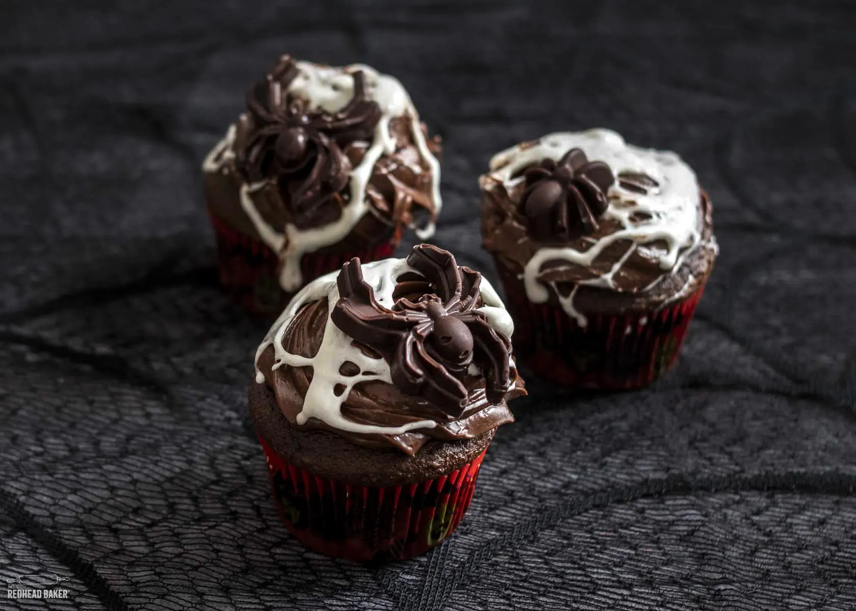 Three spiderweb cupcakes on a spiderweb tablecloth.