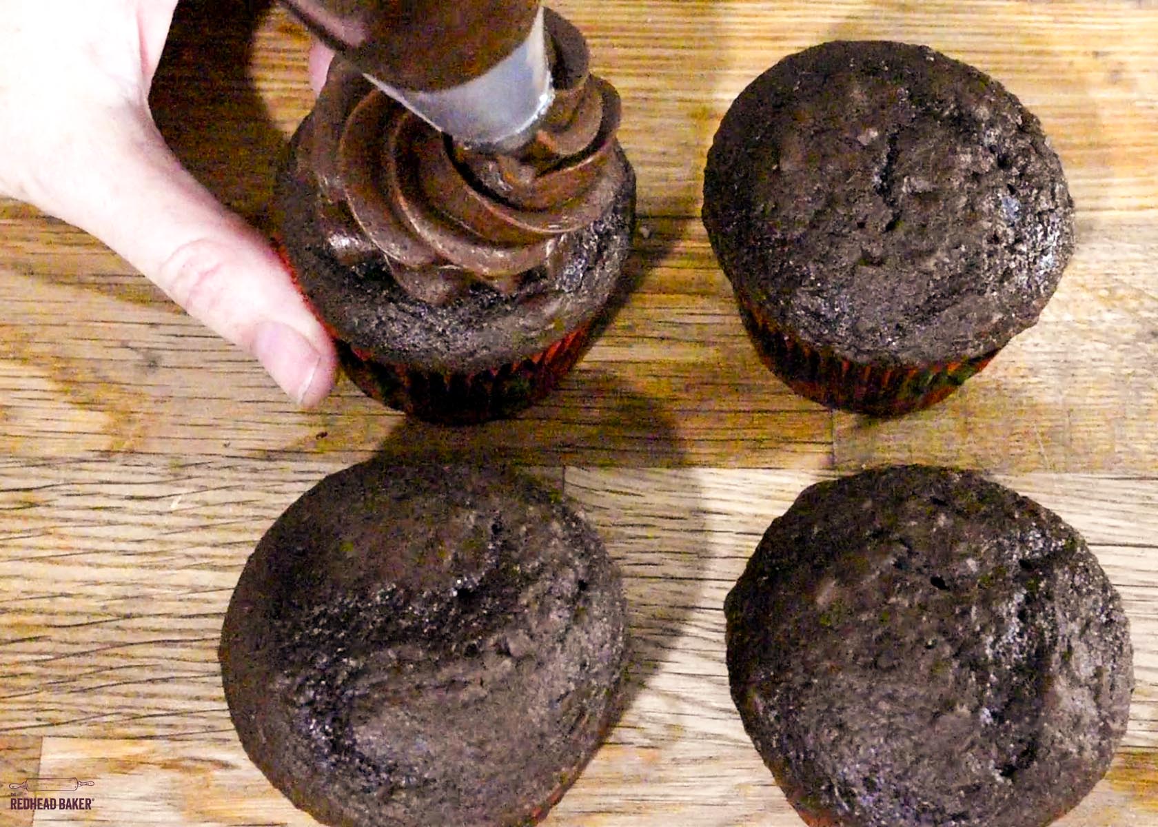 Piping a swirl of frosting onto a chocolate cupcake.