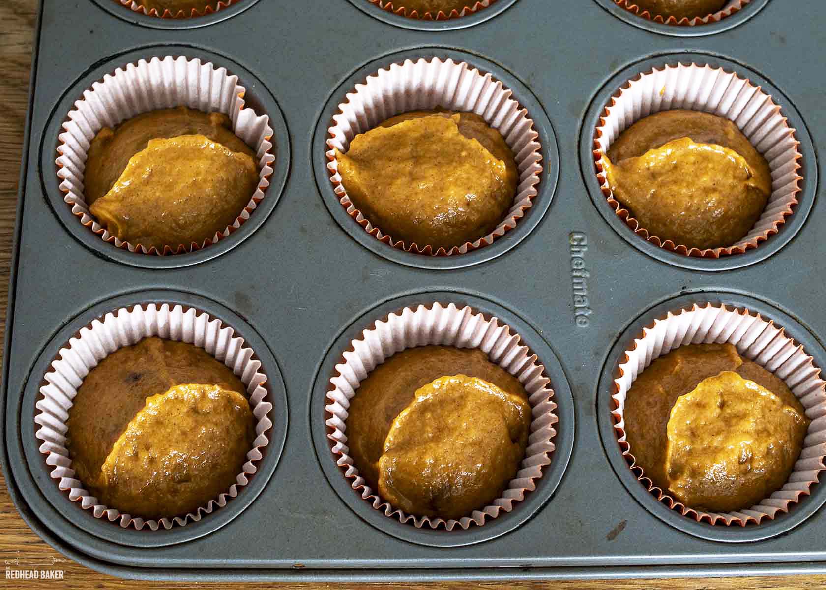 Muffin batter in paper liners in a muffin tin.