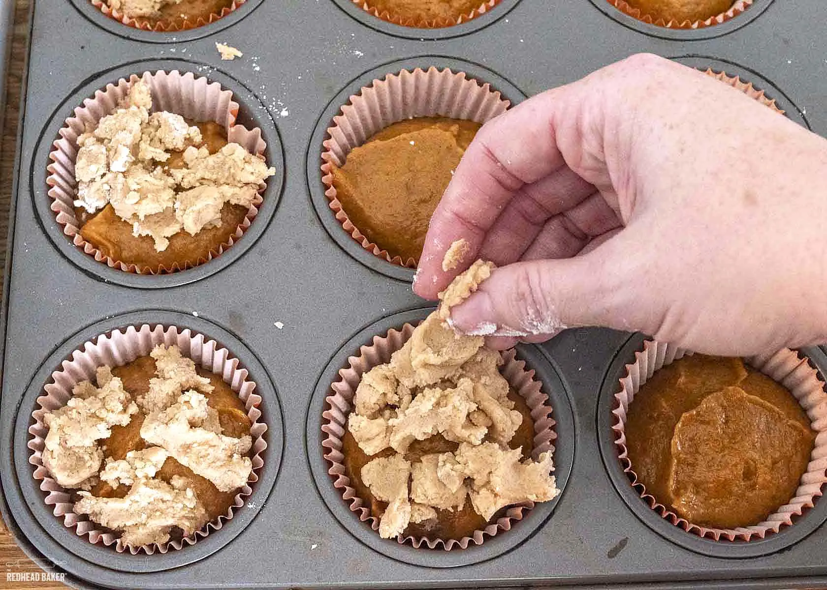 Dropping crumb topping onto muffin batter in muffin tin.