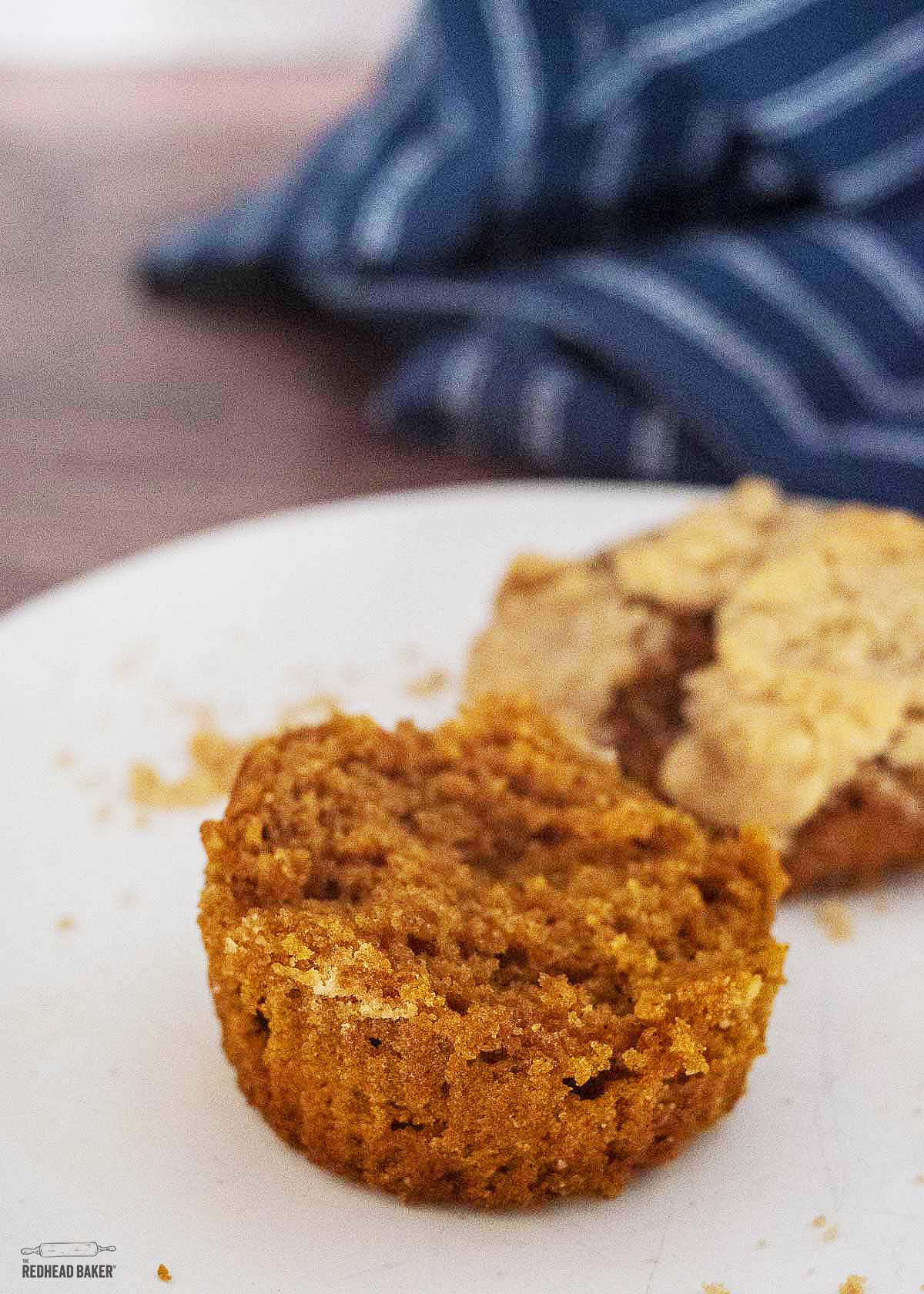 The bottom half of a pumpkin muffin in the foreground with the muffin top in the background.